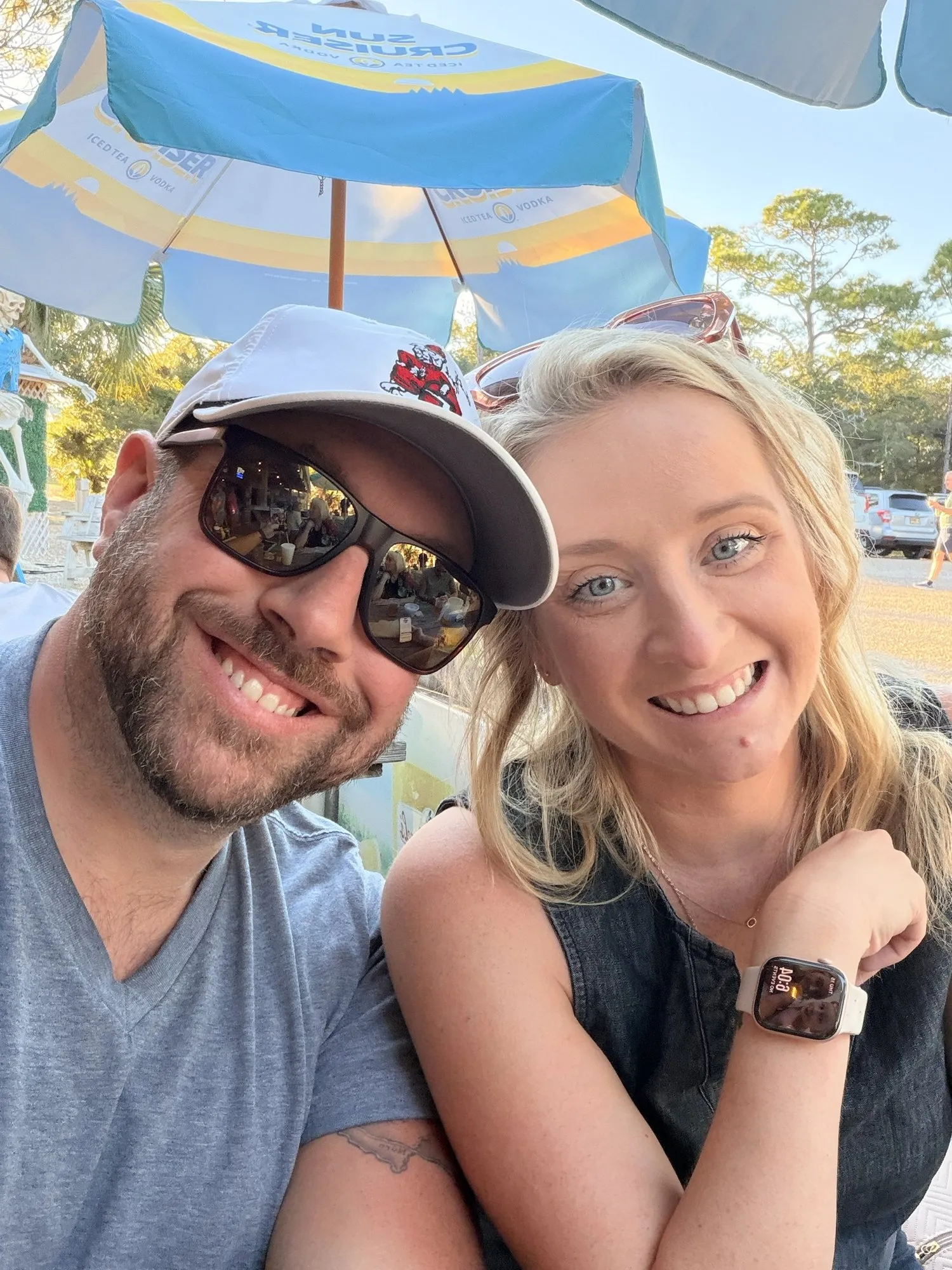 Chris and Samantha smiling under a beach umbrella
